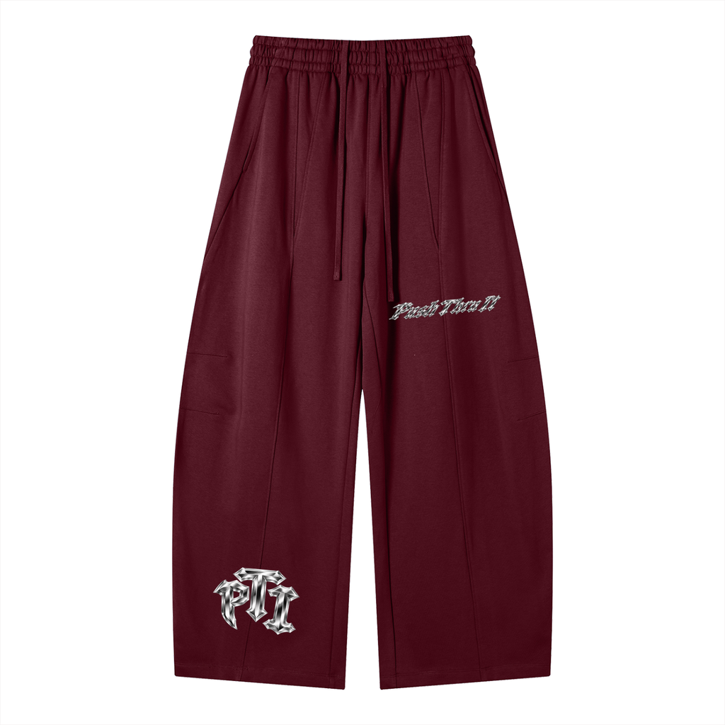 A pair of maroon wide-leg sweatpants featuring a chrome platinum embroidered 'Push Thru It' logo on the left thigh and a matching platinum color graphic on the lower left leg, displayed against a solid white background.